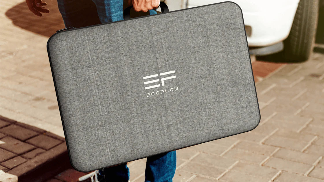 EcoFlow 220W 24V Bifacial Monocrystalline Portable Solar Panel Someone holds an Ecoflow 220W 24V Bifacial Monocrystalline Portable Solar Panel carrying case by its handle outside on a paved path beside a white vehicle.
