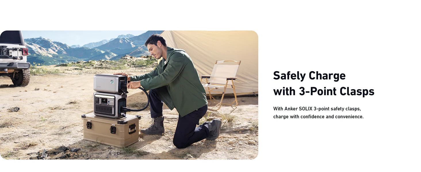 Anker SOLIX BP1000X Expansion Battery | 1,056Wh LFP (For Anker SOLIX C1000) Outdoors, a man kneels near a tent, connecting the Anker SOLIX BP1000X Expansion Battery | 1,056Wh LFP (For Anker SOLIX C1000) to a portable power station on a storage box. Mountains and a parked vehicle are behind him. Text: Safely Charge with 3-Point Clasps.