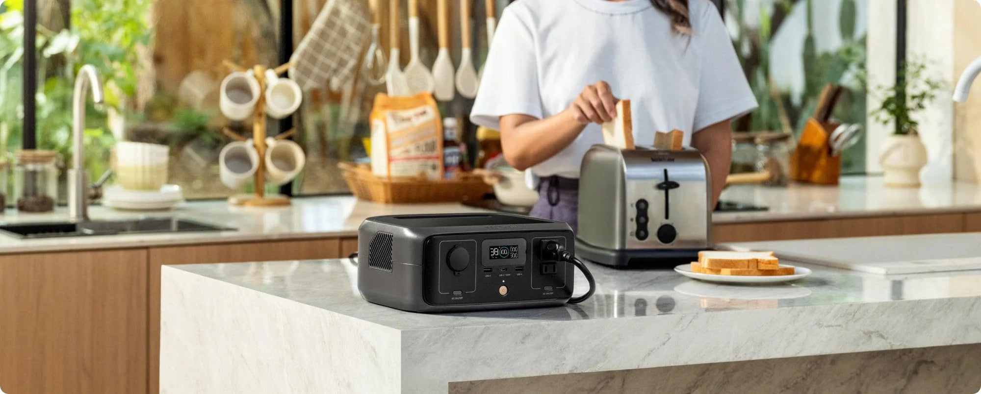 EcoFlow RIVER 3 300W 245Wh Portable Solar Power Station In a bright kitchen, a woman places bread in a toaster on a marble counter beside the EcoFlow RIVER 3 300W 245Wh Portable Solar Power Station by Ecoflow, with bread slices nearby and shelves with kitchen utensils in the background.