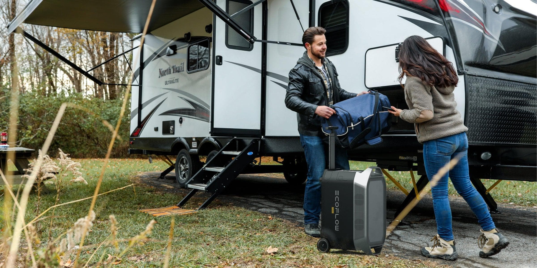 EcoFlow DELTA Pro 3600W 3.6kWh Portable Power Station + 400 Watts of Portable Solar Panels A man in a leather jacket and a woman with long hair and jeans unload their suitcase next to a parked RV in a grassy, tree-filled area, setting up the EcoFlow Delta Pro 7,200W solar panel kit for portable battery backup.