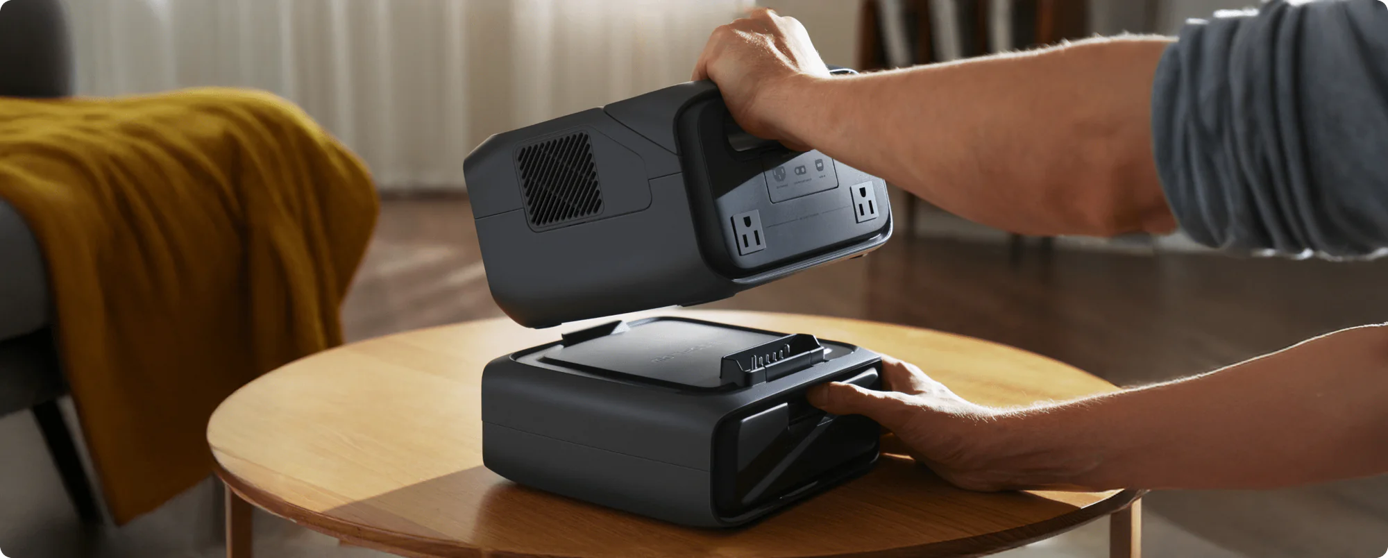 Ecoflow RIVER 3 Max 600W 572Wh Portable Solar Power Station | River 3 Plus + RIVER 3 Plus Smart Extra Battery (286Wh) A person’s hands detach the Ecoflow RIVER 3 Max 600W 572Wh Portable Solar Power Station from its RIVER 3 Plus Smart Extra Battery on a round wooden table in a cozy living room.