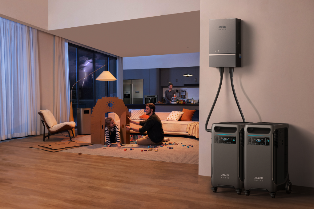 Anker SOLIX F3800 PLUS 12,000W 7.68kWh Portable Power Station with Double Voltage Hub A family relaxes in a modern living room; a man and child play with a cardboard house, while another adult is in the kitchen. Two Anker SOLIX F3800 PLUS 12,000W 7.68kWh Portable Power Stations provide backup power, with one mounted on the wall.