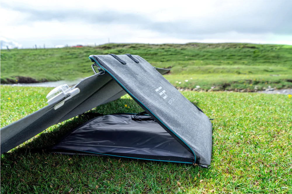 The EcoFlow 110W 24V Monocrystalline Portable Solar Panel by EcoFlow, featuring a lightweight and foldable design, is set up outdoors on grass among scenic hills, angled to capture sunlight—ideal for charging devices anywhere.